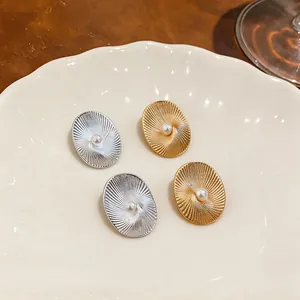 Dettaglio di orecchini ovali con trama radiale e perla centrale in oro e argento.