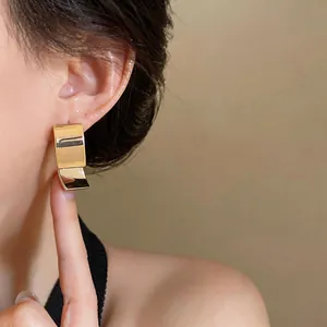 Detailopname van minimalistische 18k vergulde vierkante oorknopjes op een modeloor.