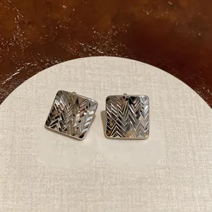 Dettaglio di orecchini a lobo quadrati color argento con elegante trama a rombi fini