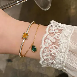 Macro view of gold bangle with square yellow stone and green teardrop pendant