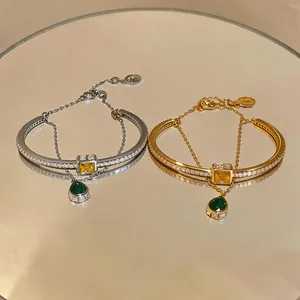 Detailed view of silver and gold double-layer bangles with green pear-shaped pendants.