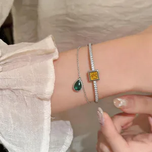 Close-up of double-layer bracelet with emerald pear pendant and yellow square gemstone