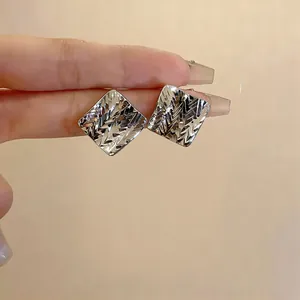 Primo piano di eleganti orecchini a lobo quadrati con trama a rombi intagliata.