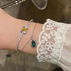 Close-up of double-layer bangle with yellow square gem and green emerald teardrop pendant