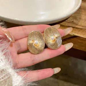 Dettaglio orecchini ovali placcati oro 18k con perla e trama a raggiera mostrati sulla mano.