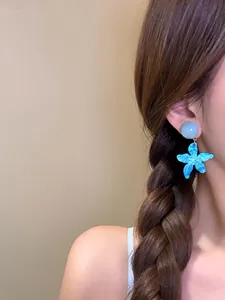 Dettaglio di un orecchino a stella marina blu indossato da una modella con treccia