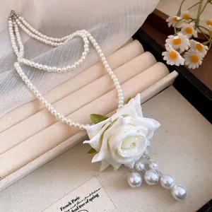 Detalle de cerca de un colgante de rosa de tela blanca y perlas en un collar de dos capas