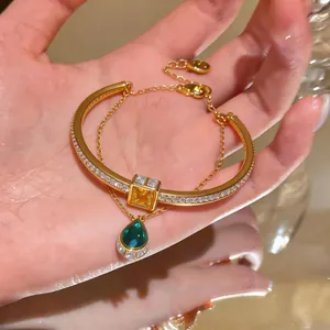 Close-up detail of a luxury gold double-layer bracelet with emerald green teardrop pendant