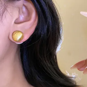 Eleganti orecchini a bottone tondi in oro spazzolato indossati da una modella chic.