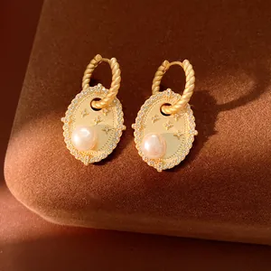 Dettaglio macro di orecchini pendenti vintage dorati con perla e motivo a stella in zircone.