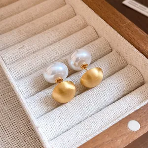 Primo piano elegante di orecchini a perno in oro spazzolato e perle in un portagioie di legno