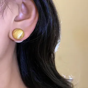 Primo piano di un elegante orecchino a bottone circolare in oro spazzolato in stile moderno
