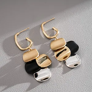 Close-up detail of modern tricolor metal dangle earrings featuring gold, black, and silver