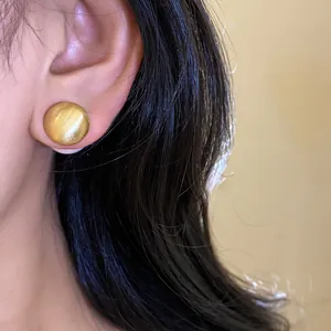 Elegante primo piano di un orecchino a lobo tondo in oro spazzolato sull'orecchio di una donna