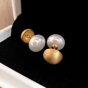 Macro di orecchini a doppia faccia con perla bianca e sfera di metallo dorato spazzolato.