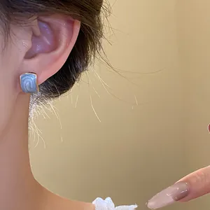 Dettaglio di un orecchino a bottone quadrato vintage in smalto blu su modella