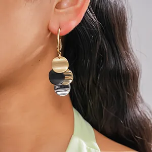 Close-up of gold-plated drop earrings with multi-colored circular discs on a model.