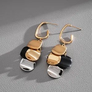 Close-up of gold-plated metal dangle earrings with mixed color sequins on grey texture