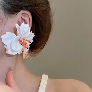 Close-up of elegant large white 3D acrylic flower earring with orange bead accents on model.