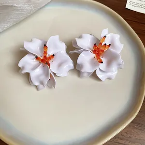 Close-up of elegant white acrylic flower earrings with vibrant orange beaded centers