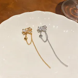 Close-up of elegant gold and silver bowknot ear cuffs featuring heart charms and tassels