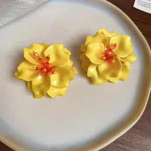 Close-up of vibrant yellow 3D acrylic flower earrings on a white ceramic plate