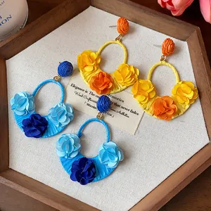 Detailed shot of bohemian raffia earrings with handmade fabric flowers in blue and yellow
