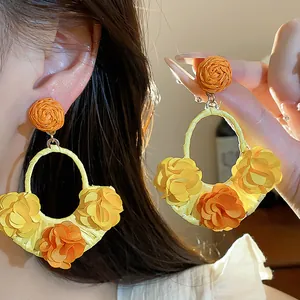 Detailed close-up showing the intricate handmade raffia flower hoop earrings in yellow and orange