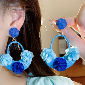 Detailed view of oversized blue raffia floral earrings showing fabric texture and style