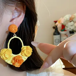 Detail view of vacation style raffia earrings with yellow and orange fabric flowers