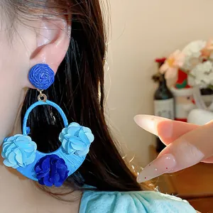 Detailed macro view of stylish blue raffia fabric flower drop earrings for vacation wear