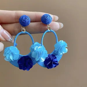 Close-up of handmade blue raffia fabric flower drop earrings for vacation style.
