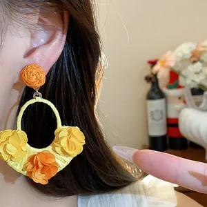 Close-up of bohemian raffia fabric flower earrings in vibrant yellow and orange colors.