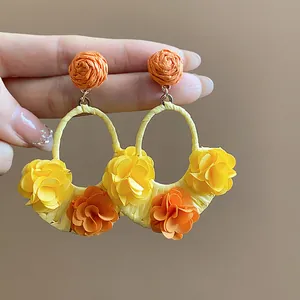 Close-up of handmade raffia earrings with vibrant yellow and orange fabric flowers