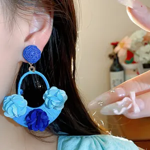 Detailed close-up showing the intricate blue raffia and fabric flower design of these earrings
