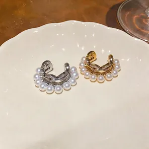 Elegant pearl and zircon non-pierced ear cuffs in gold and silver finish on a ceramic plate.