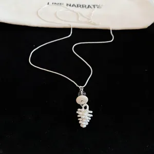 Close-up detail of a delicate white pinecone pendant necklace on a black velvet background