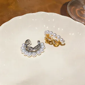Detailed macro view of luxury pearl and zircon ear cuffs in gold and silver finish on a plate