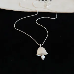 Close-up detail view of a matte silver bell-shaped pendant with dangling heart on black velvet