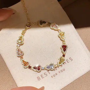 Luxurious colorful zircon heart link bracelet in gold finish resting on a beige gift pouch