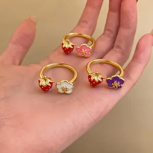 Close-up of gold adjustable rings featuring enamel strawberry and flower motifs