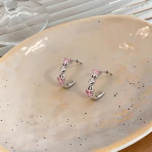 Silver C-shaped hoop earrings featuring pink heart-shaped zircons in a minimalist style.