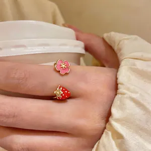 Close-up detail of an open ring featuring a pink flower and a red strawberry charm
