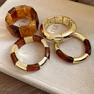 Minimalist Maillard style acrylic and gold-tone metal segmented bracelets on a vintage book