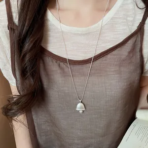 A close-up detail view of a minimalist silver bell pendant necklace on a model.