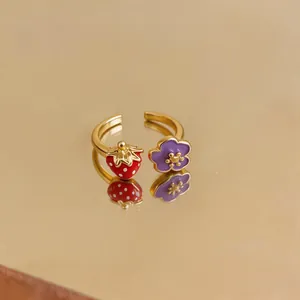 Macro view of gold-plated open ring featuring red strawberry and purple flower enamel detail