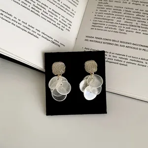 Detail view of cat-eye stone stud earrings with cascading white shell-like round discs
