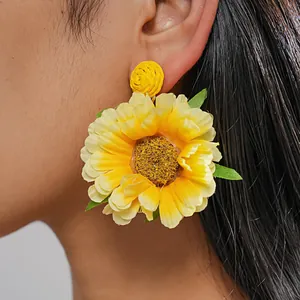Detaillierte Nahaufnahme von leuchtend gelben Baststoff-Blumenohrringen am Ohr getragen