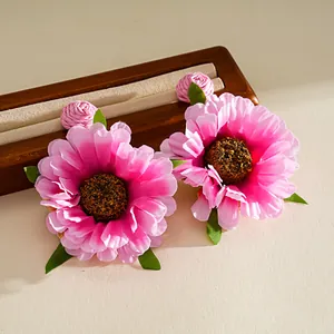 Nahaufnahme von rosafarbenen Stoffblumenohrringen im Bohème-Stil auf einem Holzschmuckständer.