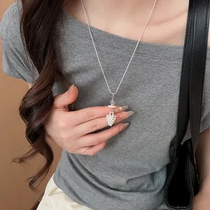 Close-up of delicate white pinecone pendant on a silver necklace worn by a model.